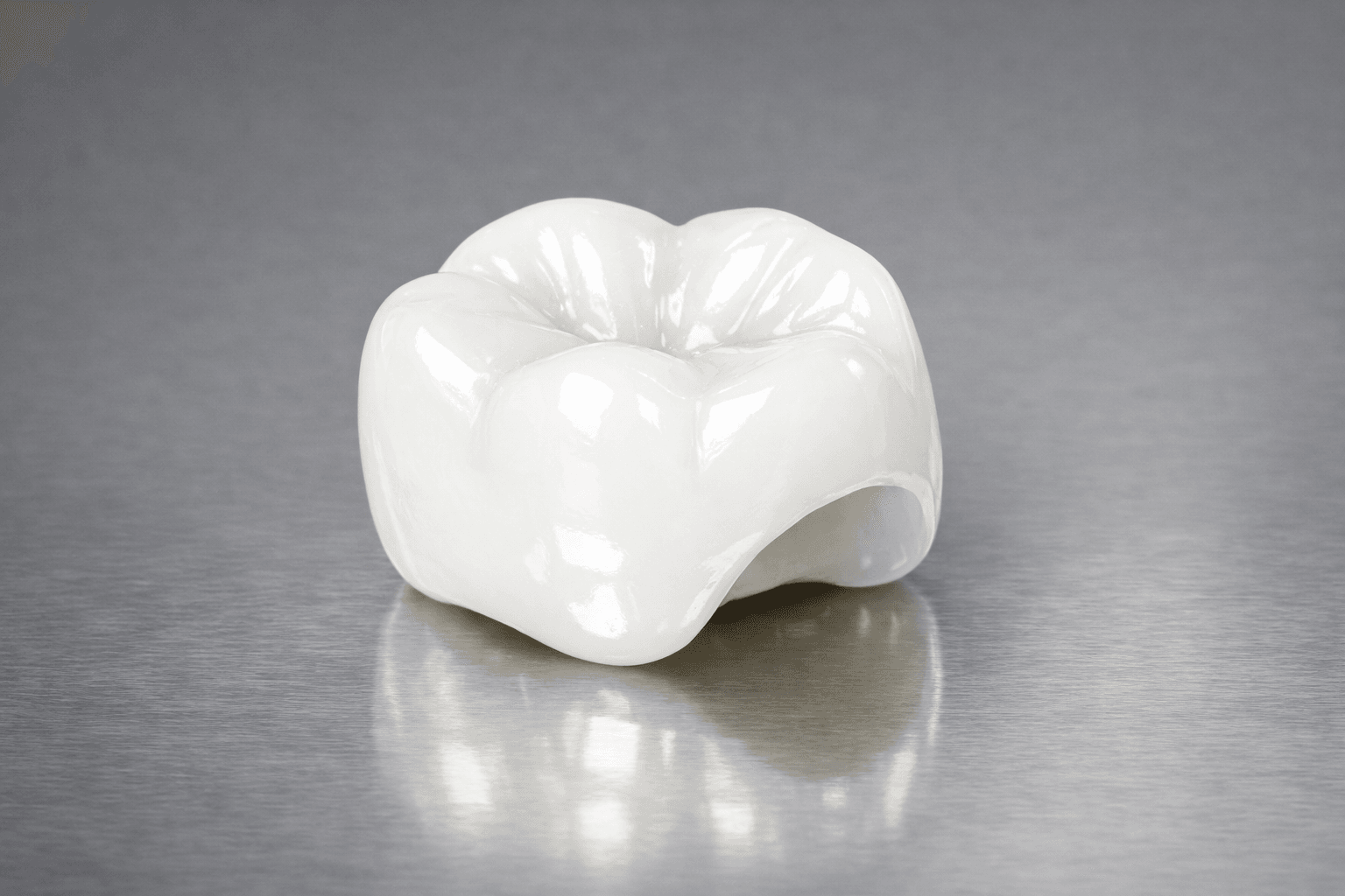 Close-up of a single ceramic molar crown on a brushed metal surface — a lab-made restoration used when a tooth has lost too much structure for a simple filling