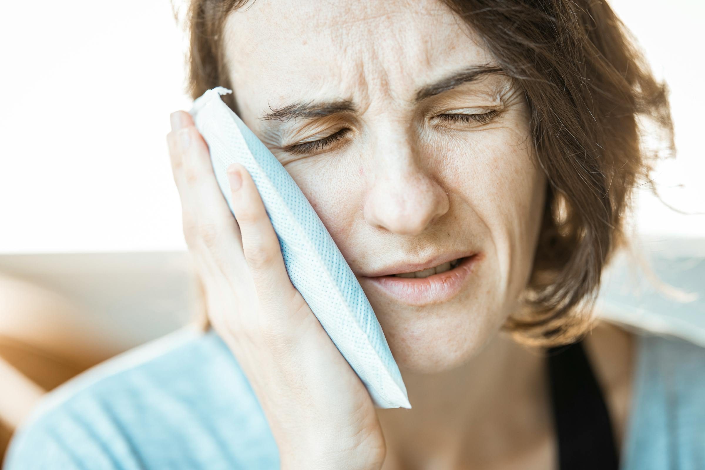 A woman calmly holding a cold compress to her cheek to manage dental pain while waiting to be seen