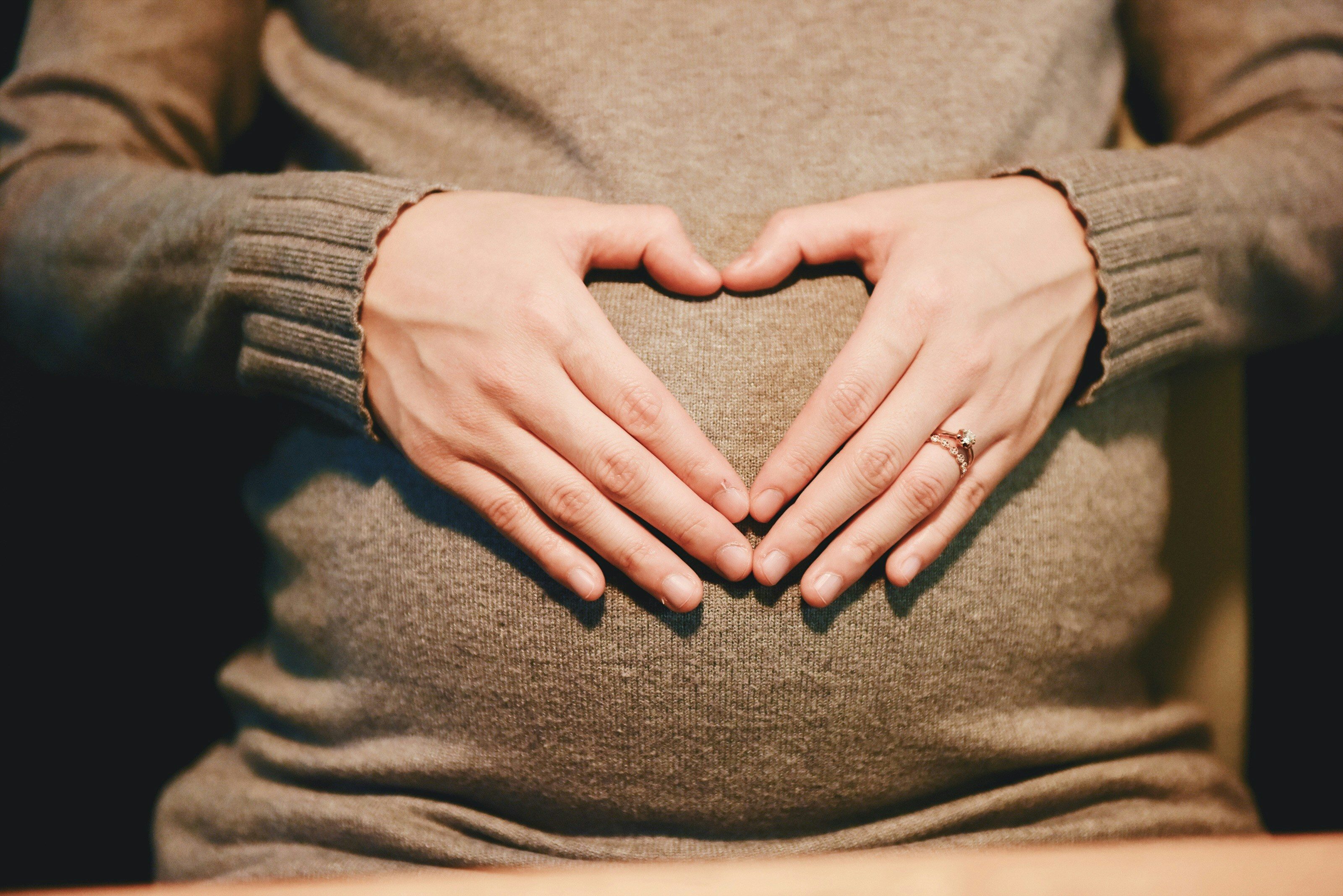 A pregnant woman's hands forming a heart over her bump — dental care during pregnancy is safe and important through every trimester