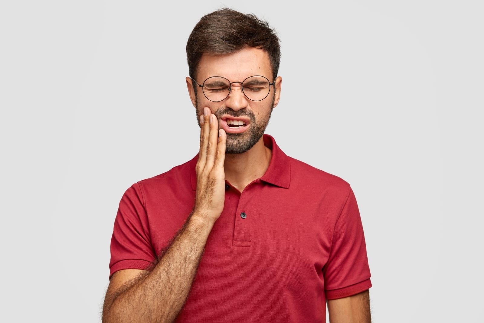Man in a red shirt wincing and pressing his hand against his cheek from sharp tooth sensitivity pain
